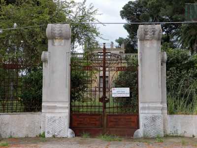 Praticamente di fronte sorge un�altra villa disabitata. L'inferriata d'ingresso, contraddistinta da un cartello di messa in affitto, ha un insolito motivo centrale che ricorda la forma di un calice ed � fiancheggiata da colonne con volute squamate